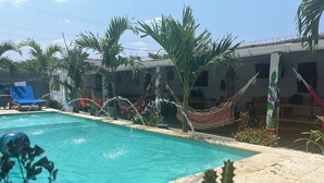 A swimming pool with clear water, surrounded by palm trees and a hammock. - Casa Playa James  (Cartagena)
