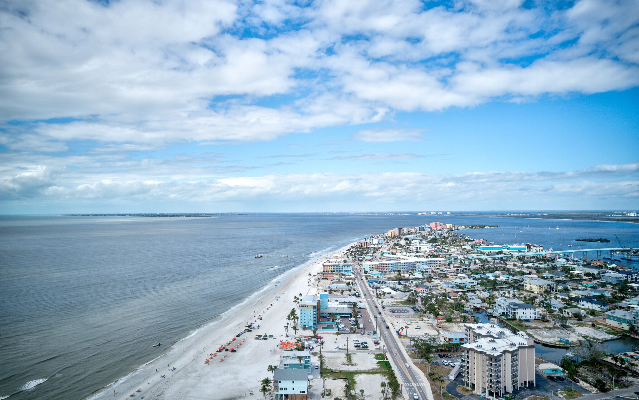 An aerial view of a coastal town with a beach, buildings, and a bridge.