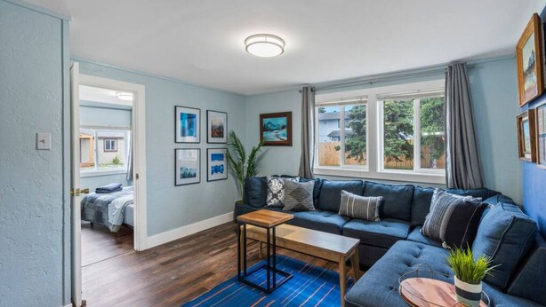 A living room with a blue sofa, a wooden coffee table, and a blue rug. There are framed pictures on the wall and a plant on the sofa. - #1 Pendleton Cottage / Midtown Hideaway / & More (Anchorage)