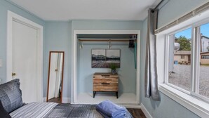 A bedroom with a bed, a wooden nightstand, a painting, and a window with a view of the outside. - #1 Pendleton Cottage / Midtown Hideaway / & More (Anchorage)