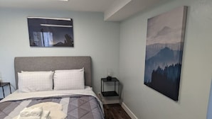 Une chambre à coucher avec un lit, des oreillers, une table de chevet et une commode, ainsi qu’un tableau accroché au mur.