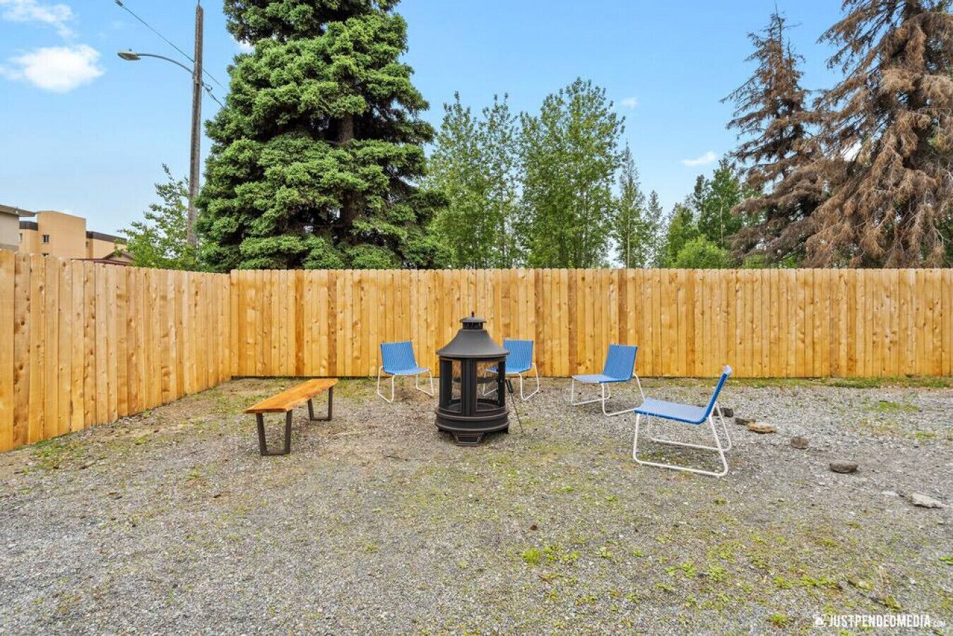 A backyard with a wooden fence, a bench, and two blue chairs.