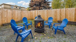 A backyard with a wood-burning stove, four blue Adirondack chairs, and a wooden fence. - Historic cottage - 10 minute walk to restaurants & trails (Anchorage)