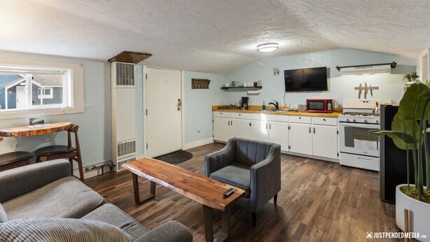 A compact living space with a kitchenette, a dining area with a wooden table, and a gray armchair. - Historic cottage - 10 minute walk to restaurants & trails (Anchorage)