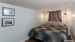 A bedroom with a bed, two framed pictures on the wall, and two hanging light fixtures. - Historic cottage - 10 minute walk to restaurants & trails (Anchorage)