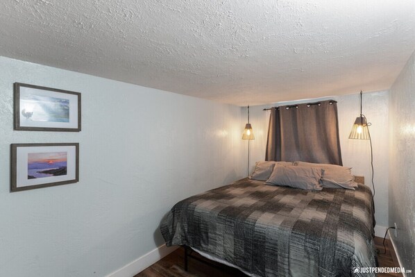 Un dormitorio con una cama, dos cuadros en la pared y dos lámparas colgantes.