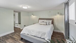 A bedroom with a bed, bedside lamps, a ceiling light, and a door with a curtain. - Walking distance to restaurants, trails, and cafes.  10 min. uber from airport. (Anchorage)