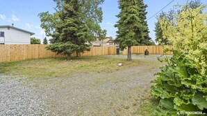 A fenced backyard with two tall trees, a gravel path, and a wooden fence. - Walking distance to restaurants, trails, and cafes.  10 min. uber from airport. (Anchorage)