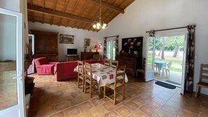 A spacious living area with a wooden ceiling, a dining table set for four, a red sofa, and a kitchen area with a cabinet and a television. - 085 - Invitation to rest in this villa in Grande Combe (SOULAC SUR MER)