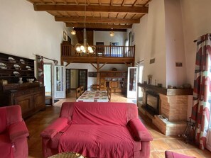A spacious living room with a red sofa, wooden beams, a fireplace, and a high ceiling. - 085 - Invitation to rest in this villa in Grande Combe (SOULAC SUR MER)