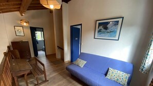 A cozy room with a wooden dining table, a blue sofa with patterned cushions, and a framed painting on the wall. - 085 - Invitation to rest in this villa in Grande Combe (SOULAC SUR MER)