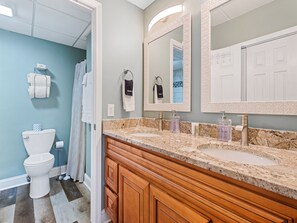 A bathroom with a white toilet, a sink with a granite countertop, and wooden cabinets.