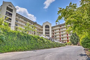 A multi-story apartment building with balconies, surrounded by greenery and a clear sky.
