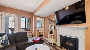 Ein Wohnzimmer mit Kamin, Fernseher, Bücherregal und großem Fenster.