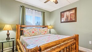 Ein Schlafzimmer mit hölzernem Bettgestell, floralem Bettbezug, Deckenventilator und einem Vorhangfenster.