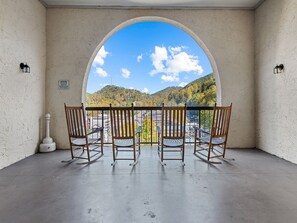 Un balcon avec quatre fauteuils à bascule en bois, donnant sur un paysage pittoresque comprenant une montagne et une ville.