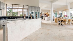 A spacious kitchen with a large island, grey cabinets, and a view of palm trees outside.