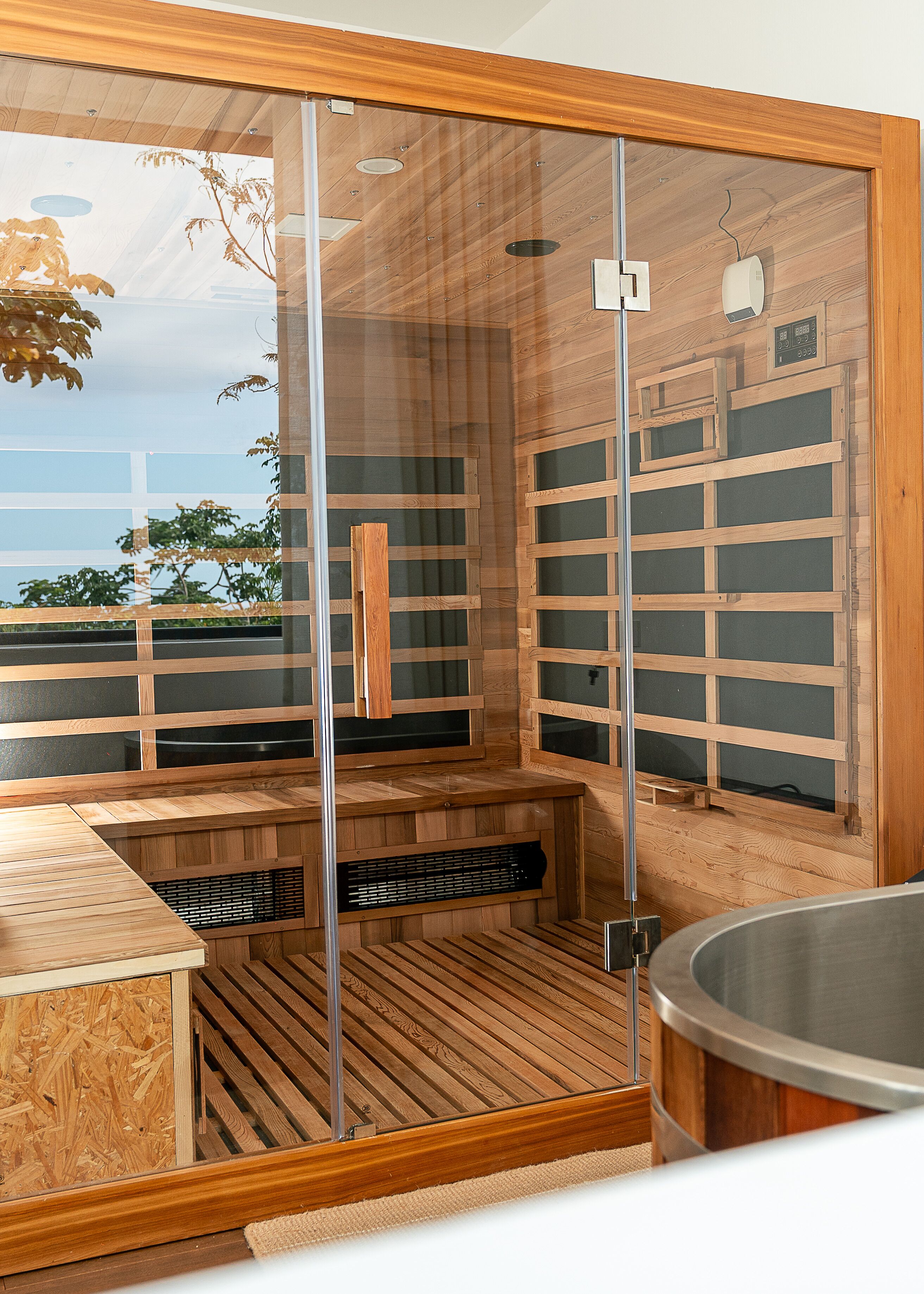 Un sauna avec des bancs en bois, une porte en verre et une vue sur les arbres.