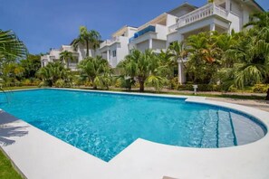 Una piscina rodeada de vegetación exuberante y edificios blancos con balcones.