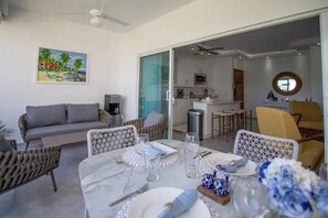 Un comedor con una mesa preparada para cuatro, un sofá y una cocina al fondo.