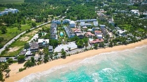An aerial view of a coastal resort with multiple buildings, a sandy beach, and turquoise waters. - 3BR Renovated Beachfront Condo + Cooking/Cleaning (Las Terrenas)
