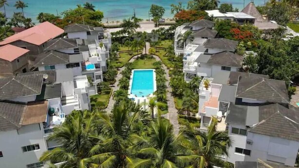 A residential area with a central swimming pool surrounded by houses, a clear view of the ocean, and palm trees. - 3BR Renovated Beachfront Condo + Cooking/Cleaning (Las Terrenas)