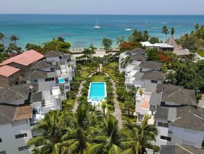 Zona residencial con piscina central rodeada de casas, vista despejada al océano y palmeras.