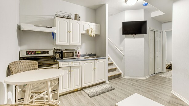 Cocina compacta con armarios blancos, microondas y un pequeño comedor con sillas de mimbre.