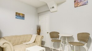 Una sala de estar con un sofá color beige, una mesita blanca, dos sillas de mimbre y una puerta blanca.