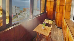 Un balcón con mobiliario de madera, ventanas amplias y vistas a edificios.