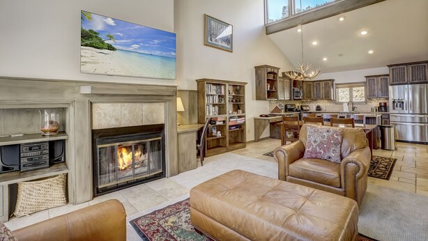Amplia sala de estar con chimenea, sofás de cuero, una estantería y una cocina al fondo.
