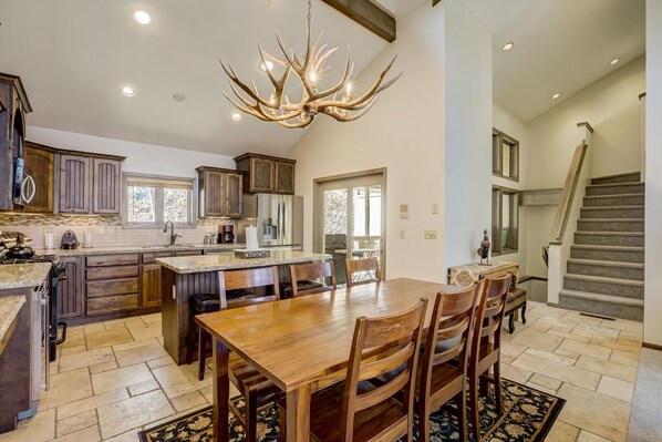 A spacious kitchen with dark wooden cabinets, a large island, and a chandelier.