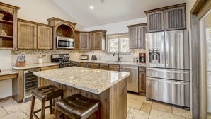 Cocina con gabinetes de madera, electrodomésticos de acero inoxidable, encimera de granito y una isla integrada con taburetes de bar.