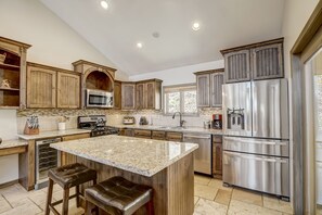 Cocina con gabinetes de madera, electrodomésticos de acero inoxidable, encimera de granito y una isla integrada con taburetes de bar.