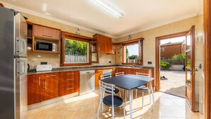 A kitchen with wooden cabinets, a microwave, a dishwasher, and a dining table with chairs. - Villa Can Tosam Meiga with Wi-Fi, Pool, Terraces & Balcony (Cales de Mallorca)