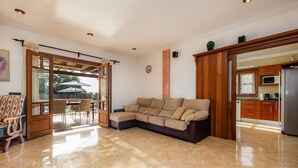 A spacious living area with a sectional sofa, a dining table with chairs, a kitchen with cabinets and appliances, and a sliding glass door leading to an outdoor patio. - Villa Can Tosam Meiga with Wi-Fi, Pool, Terraces & Balcony (Cales de Mallorca)