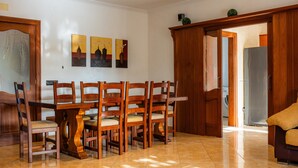 A dining area with a wooden table and chairs, a kitchen in the background, and a door leading to another room. - Villa Can Tosam Meiga with Wi-Fi, Pool, Terraces & Balcony (Cales de Mallorca)