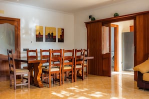 Comedor con mesa y sillas de madera, cocina al fondo y puerta que da a otra habitación.