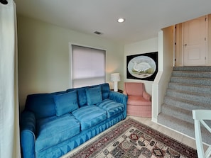 A living room with a blue sofa, a patterned rug, a red armchair, a lamp, and a staircase. - Tybee Stars by Tybee Vacation Rentals (Tybee Island)