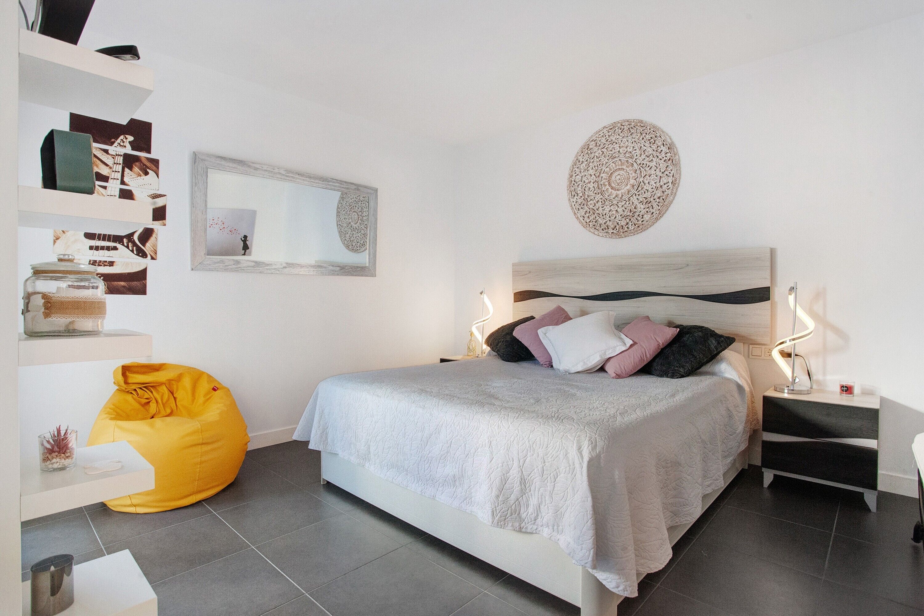 Un dormitorio moderno con cama, mesitas de noche, un sillón de pie y decoración en la pared.