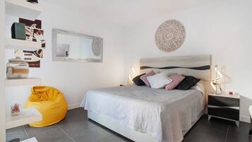Un dormitorio moderno con cama, mesitas de noche, un sillón de pie y decoración en la pared.