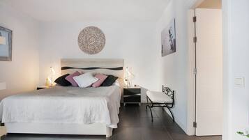 Un dormitorio con cama, mesitas de noche, un banco y una puerta.