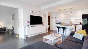 A modern living room with a flat-screen TV, a sofa, a coffee table, and a kitchen area with bar stools. - Vacation Home 'The Garden Secret' with Shared Pool, Private Terrace and Wi-Fi (Villaverde)