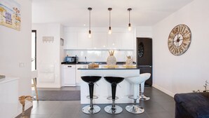 A modern kitchen with white cabinets, a central island with bar stools, pendant lighting, and a clock on the wall. - Vacation Home 'The Garden Secret' with Shared Pool, Private Terrace and Wi-Fi (Villaverde)