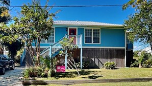 A two-story house with a blue exterior, a red front door, and a small porch with a white railing. - Saltcreek Sunsets by Tybee Vacation Rentals (Tybee Island)