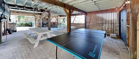 A ping pong table in a covered outdoor area with picnic tables and a wooden fence.