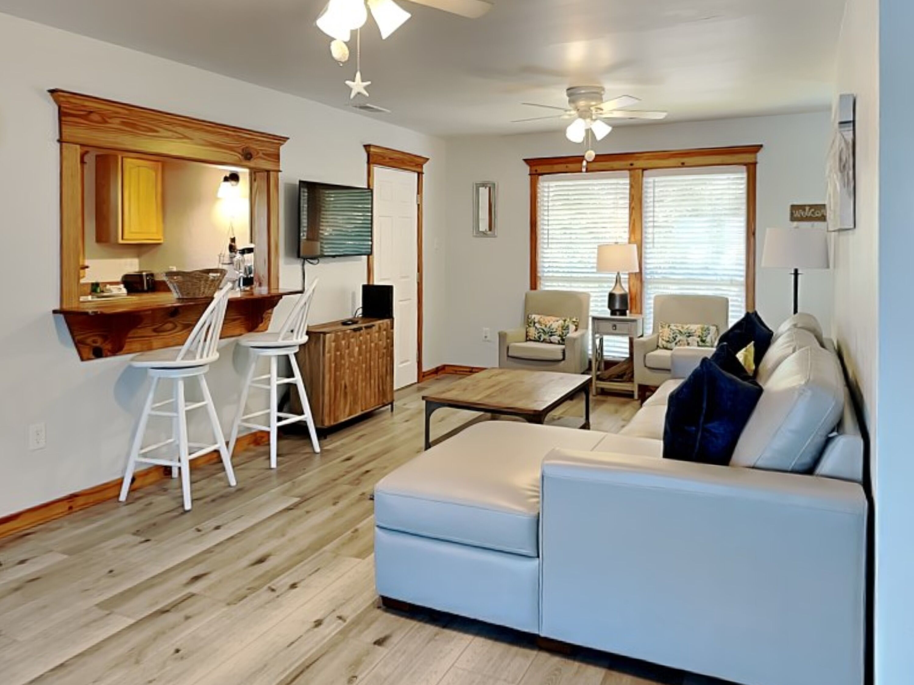 A living room with a sofa, chairs, a coffee table, and a kitchen area with a bar and stools.
