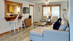 A living room with a sofa, chairs, a coffee table, and a kitchen area with a bar and stools. - Saltcreek Sunsets by Tybee Vacation Rentals (Tybee Island)
