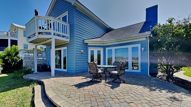 A two-story house with a balcony, a patio with outdoor furniture, and a large window overlooking the yard.