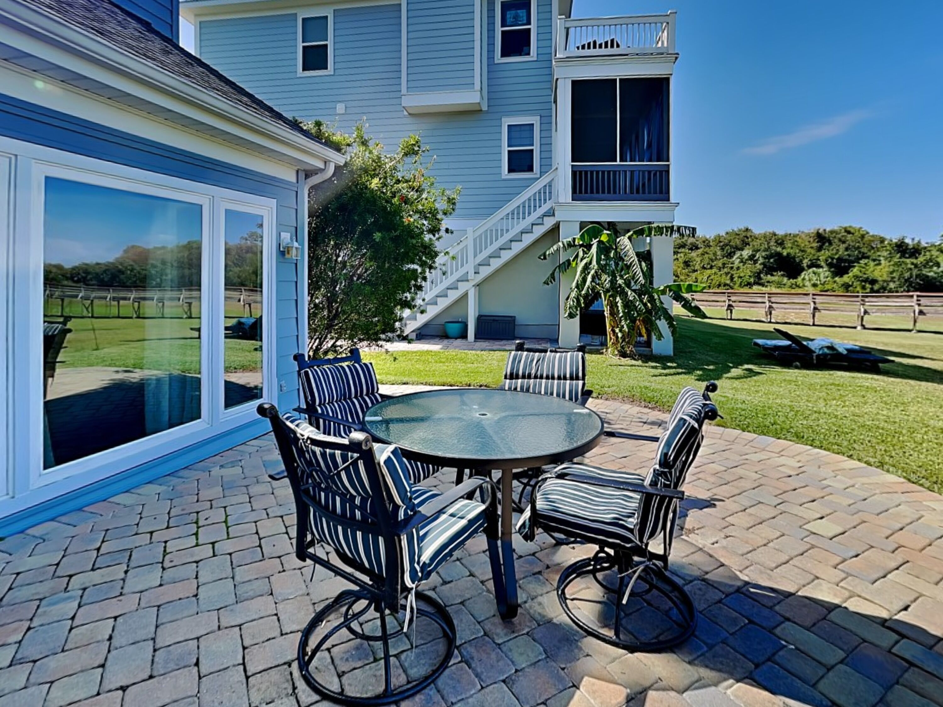 A patio with a round table and four chairs, a covered area with a glass door, and a staircase leading to a balcony.
